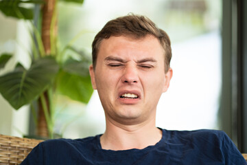 a middle-aged man with a disgruntled face sneezes. 