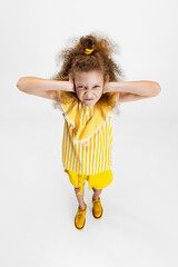 High angle view of little cute curly preschool beautiful girl closes ears with hands isolated over white studio background.