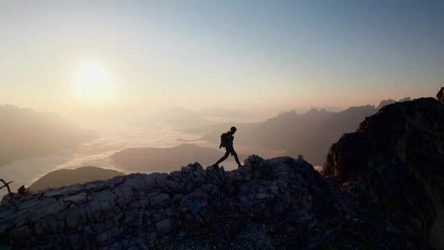 A mountaineer is hiking on a ridge and looking towards the sunrise.  Aerial footage was taken in the Dolomites - Italy.