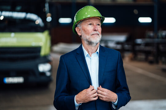 Businessman wearing green hardhat while standing in factory