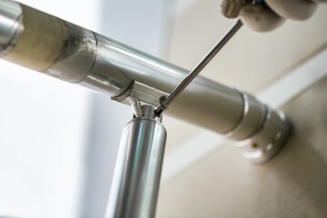 A worker in gloves repairs a metal railing of a staircase using a screwdriver and a drill