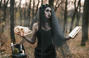 Brunette witch girl conjures in the forest conducts rituals with a fantasy skull nature magic in...