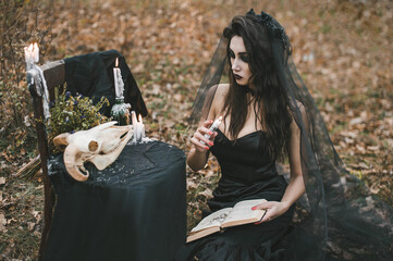 Brunette witch girl conjures in the forest conducts rituals with a fantasy skull nature magic in...
