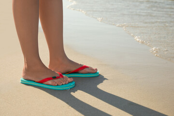 Fototapeta na wymiar Woman wearing flip flops on sandy beach, closeup