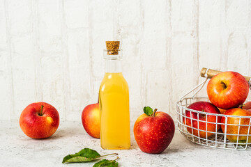 Frischer Apfelsaft in einer Glas Flasche und rote Äpfel in einem Korb auf einem weißen rustikalen Tisch. Herbst.