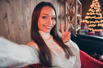 Photo of adorable shiny young lady wear white pullover smiling taking selfie showing v-sign indoors house home room