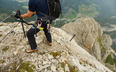 via ferrata climber with full gear, climbing harness, backpack and mountain boots high above the valley ground in italian dolomites, South Tyrol