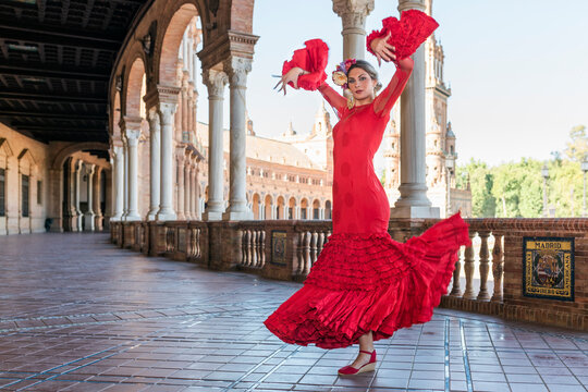 Female flamenco artist dancing with hands raised on walkway at Plaza De Espana, Seville, Spain