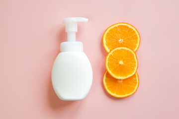 White unbranded bottle with pump and orange slices on light pink background. Blank container for lotion, cream, sunscreen, shampoo or hair conditioner. Mockup style, cosmetic products advertising