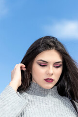 Fototapeta premium brunette woman looking down with l amno in her hair and a gray woolen dress and blue sky in the background