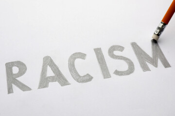 Erasing word Racism written on paper sheet with pencil, closeup