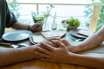 Hands of young affectionate couple sitting by served table while having dinner or breakfast