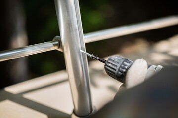 A worker in gloves repairs a metal railing of a staircase using a screwdriver and a drill