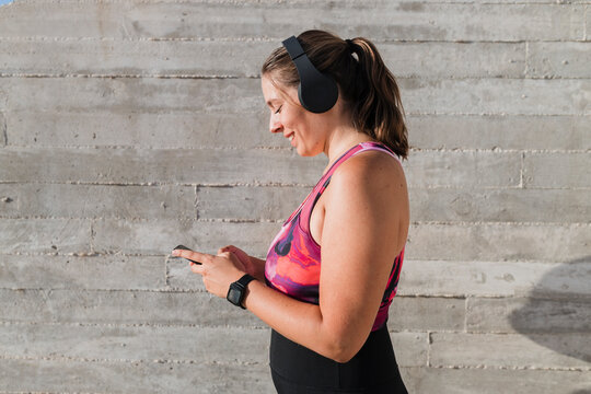 Smiling sportswoman wearing wireless headphones while listening music by wall - Powered by Adobe