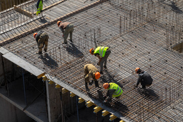 builders in hard hats and protective vests work at the construction site of a multi-storey...