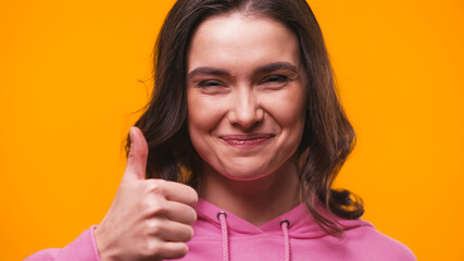 happy woman showing thumb up while looking at camera isolated on yellow