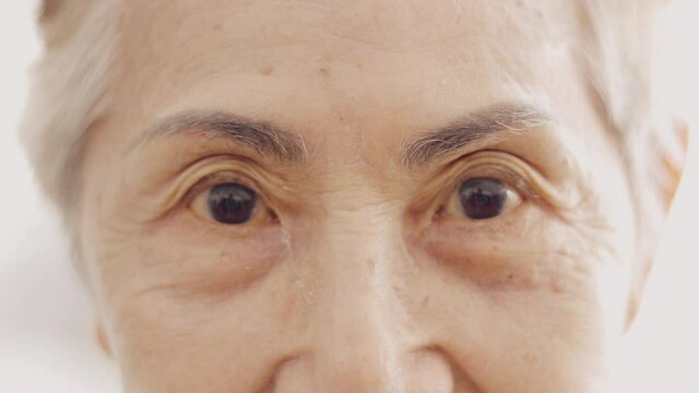 Face close up and 4K slow motion of asian senior lady who is 80 years old grandmother with high key style of bright background shows beautiful detail of wrinkle skin, black eyes and grey hairs.