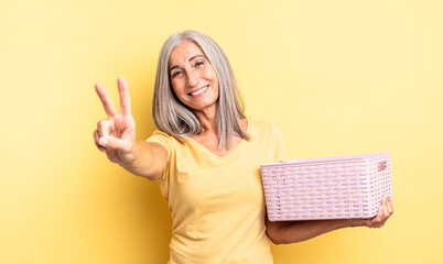 middle age pretty woman smiling and looking friendly, showing number two. empty basket concept