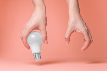 Breast Cancer Awareness Month. Female hands holding an electric light bulb on a pink background. Close up. The concept of oncology