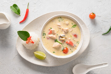 Spicy creamy coconut Tom Kha Gai soup with chicken, cherry tomato, coconut milk, kaffir, galangal, lemongrass,mushrooms on light background. Asian Thai food. Coconut Chicken Soup.