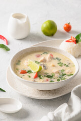 Spicy creamy coconut Tom Kha Gai soup with chicken, coconut milk, galangal, lemongrass,mushrooms on light background. Asian Thai food. Vertical format. Coconut Chicken Soup.