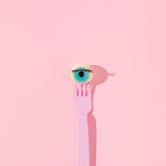Creative layout with eyeball figurine on pink fork on pastel pink background. Halloween aesthetic...