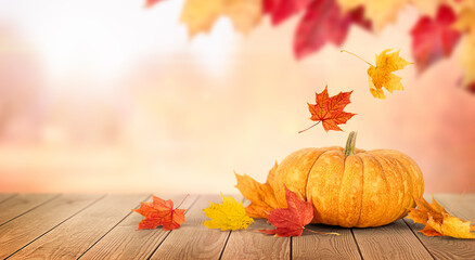 Fototapeta na wymiar pumpkin and falling autumn leaves on a wooden table