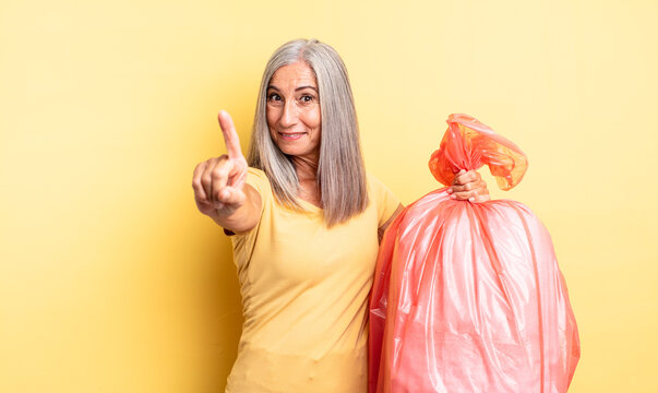 middle age pretty woman smiling proudly and confidently making number one. plastic garbaje bag