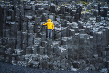 Man wearing yellow coat looking up at Reynisdrangar basalt columns at Reynisfjara Beach, Iceland