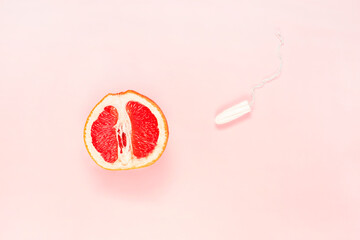 Fototapeta premium Half of fresh grapefruit and tampon on pink background. Symbol of vagina. Gynecology, female intimate health, menstruation concept.