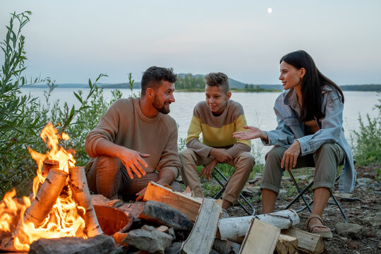 Young man and woman having discussion by campfire while their son sitting between them