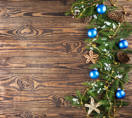 Fir branches decorated with blue Christmas balls, cones and a garland on a brown background. Christmas and New Year concept. Horizontal orientation, copy space, top view.
