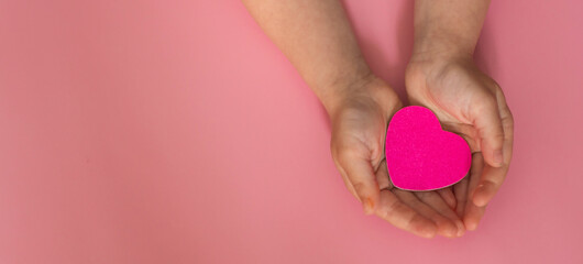 hands hold a pink heart on a pink background. hope, love, prosperity, family insurance, World Heart...