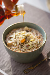 pouring maple syrup over a bowl of oatmeal with different toppings 