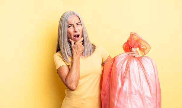 middle age pretty woman with mouth and eyes wide open and hand on chin. plastic garbaje bag