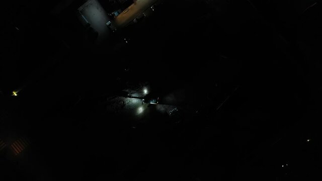 Aerial view above a heavy machinery with lights on demolishing a building in middle of a city - rising, top down, drone shot