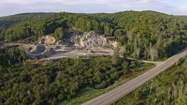 Drone shot flying over rural Ontario highway to view open pit granite mine cut out of hillside