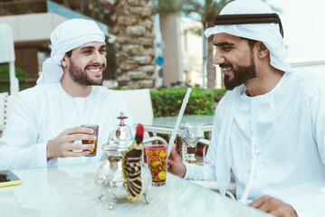 Fototapeta na wymiar Two young businessmen going out in Dubai. Friends wearing the kandura traditional male outfit in Marina