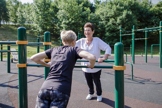 Female friend exercising while leaning on parallel bars during sunny day