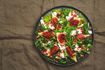 Fig salad with white cheese, walnuts, arugula and jam dressing on rust green background, top view, copy space