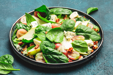 Salad with pear, blue cheese, spinach, grapes, walnuts on blue background, top view, copy space