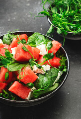 Watermelon salad bowl with soft goat cheese, spinach and pea sprouts on gray background, top view, copy space