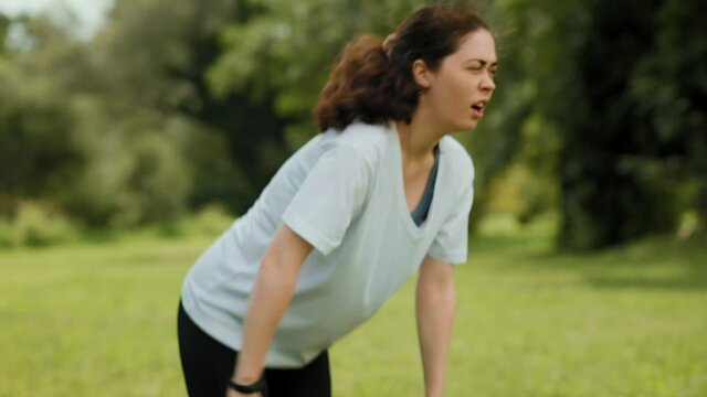 Sports injury. A young woman in sportswear doing forward bents, and clutches her back in pain. Close up. Outdoors warmup.