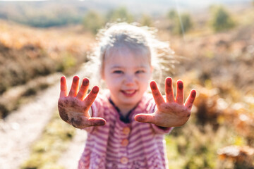 Smiling happy girl showing dirty hands after playing on the ground