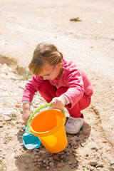 girl with glasses playing with a blue shovel and yellow bucket