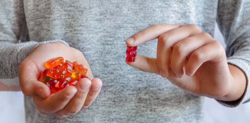 The child holds colored jelly bears in his hands and shows one. Close-up. Vitamins for kids, favorite gummy candy concept.