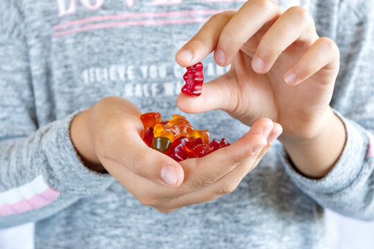 A girl holds a gummy bear in her hand, wants to eat jelly sweets. Close-up. Concept of children's delicacy, unhealthy food, vitamins for kids.