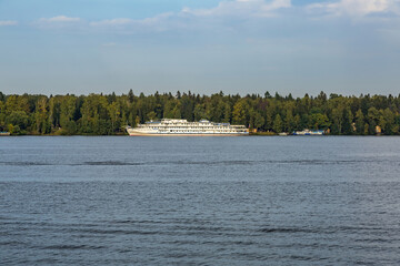 White three-deck ship on a river cruise. The vessel is moored by the green forest