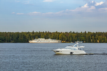 White three-deck ship on a river cruise. The vessel is moored by the green forest
