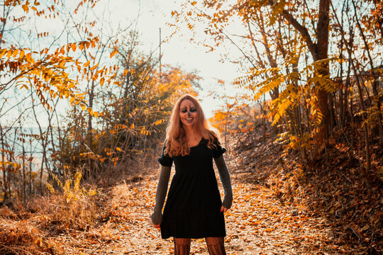 Smiling woman with Halloween make-up standing in forest during autumn - Powered by Adobe